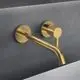 Wandarmatur in gebürstetem Gold mit runder Rosette, installiert an einer grauen Wand. Ideal Standard-Logo auf der Rosette sichtbar.